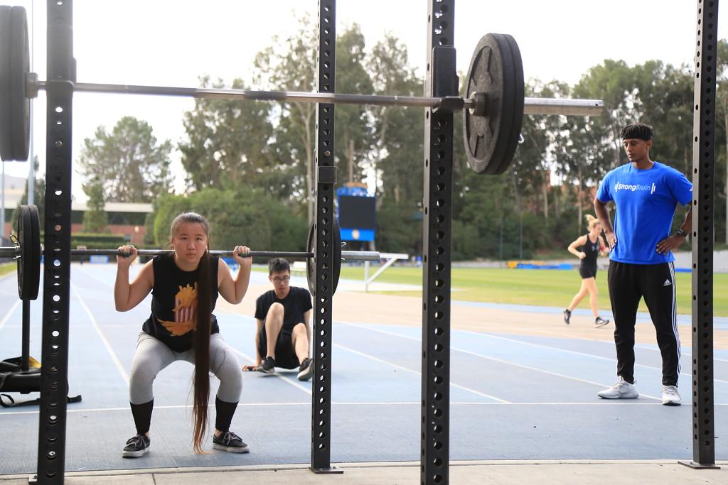 girl squatting with a barbell outside with an instructor